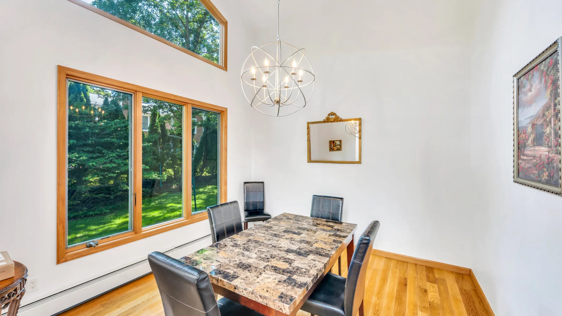 Comedor con una mesa rectangular, sillas y grandes ventanas con vistas a la vegetación.