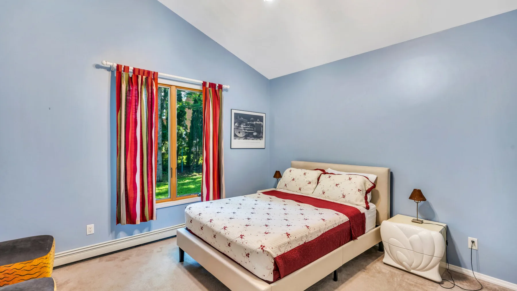Un dormitorio con una cama vestida de rojo y blanco junto a una ventana con cortinas.