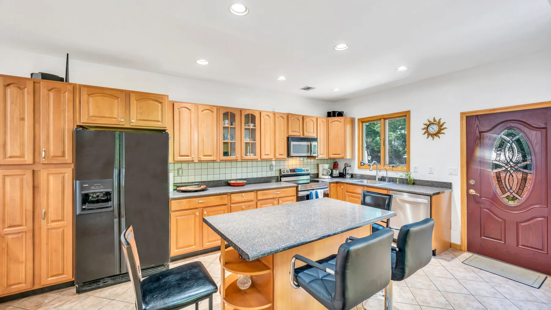 Una cocina luminosa con gabinetes de madera, una isla central y un refrigerador oscuro.