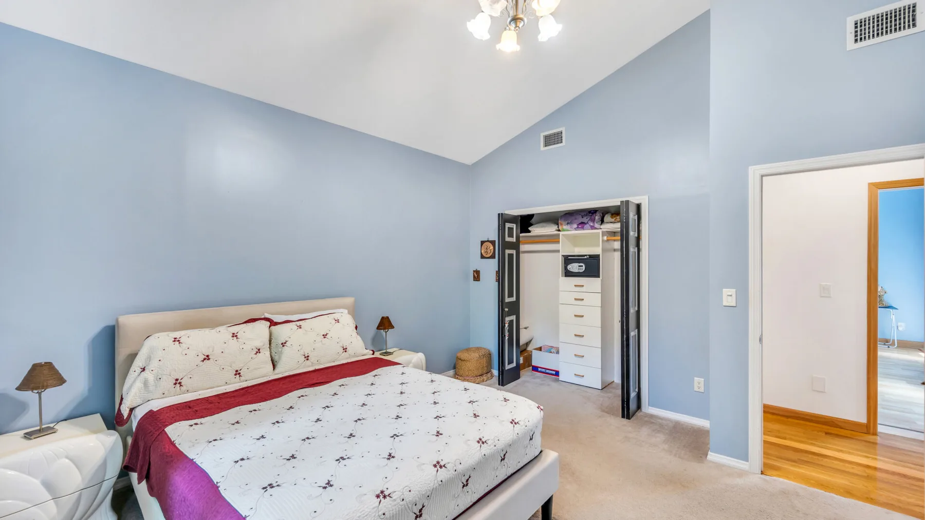 Un dormitorio con una cama cubierta con ropa de cama clara y estampada y un armario abierto.