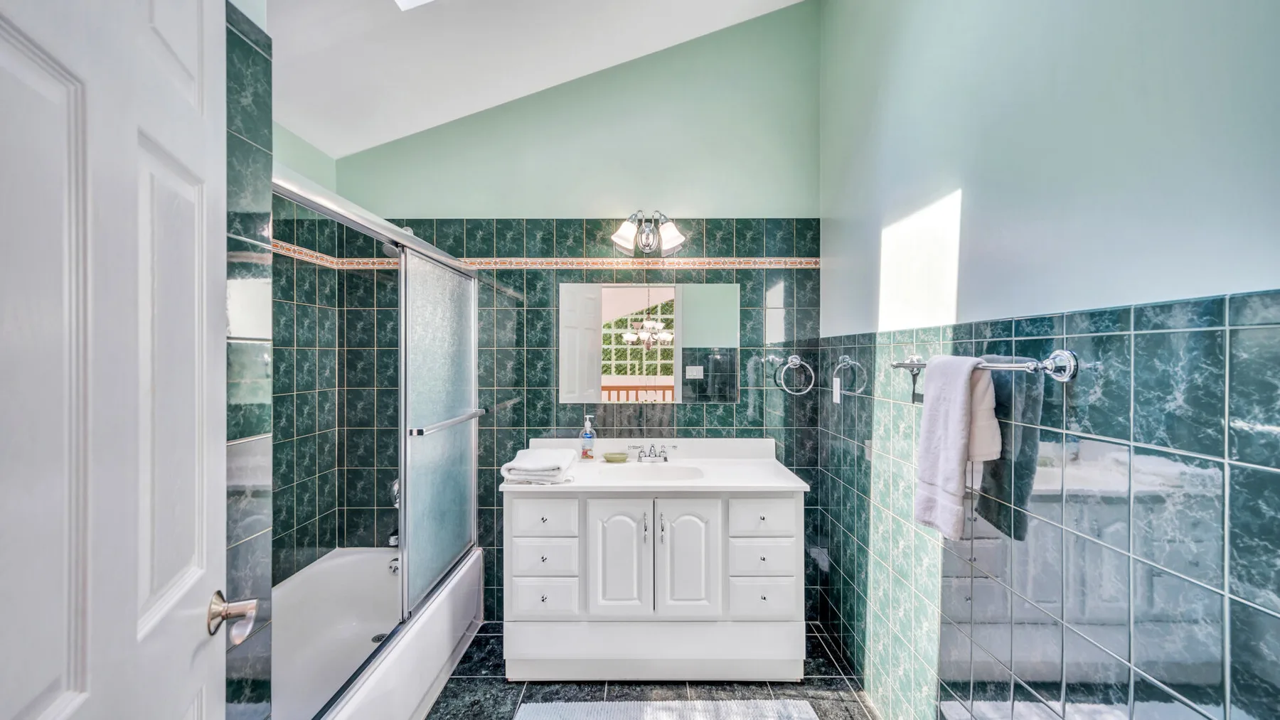 Un baño alicatado con bañera, mampara de ducha de vidrio y lavabo blanco.