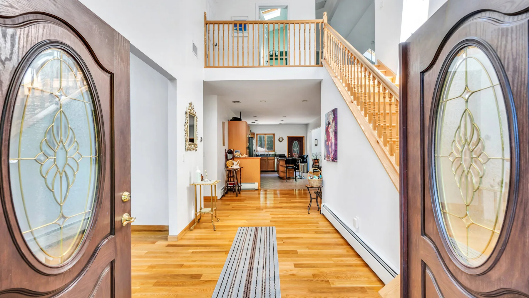 Una entrada da paso a una sala luminosa, con una escalera de madera a un lado.