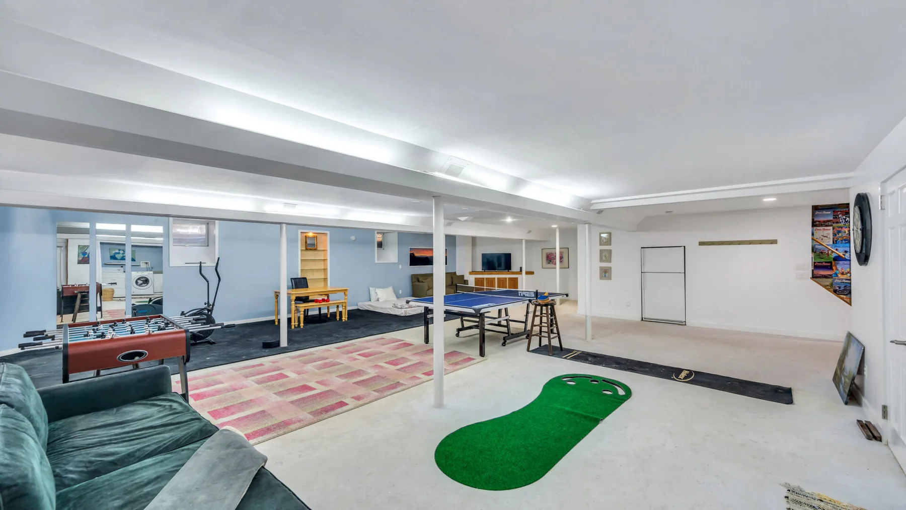 Una sala de recreo en el sótano con mesas de juego, asientos y una alfombra verde de putting.