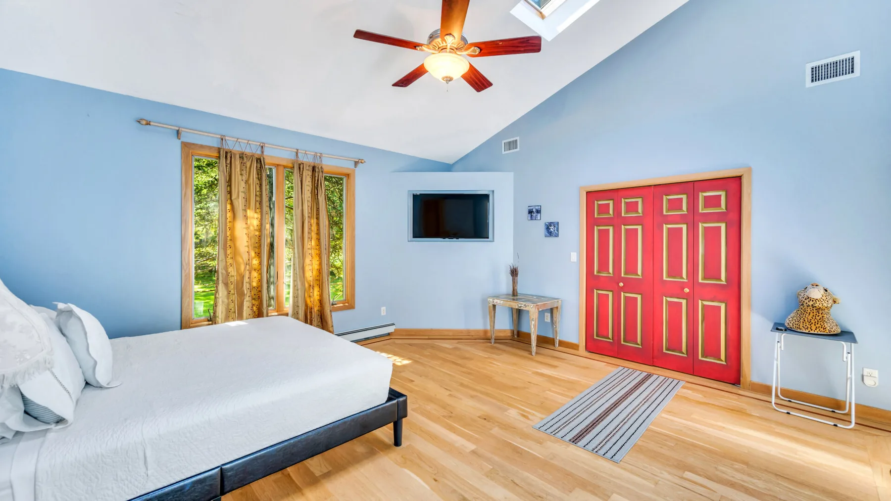 Un dormitorio luminoso con una cama grande, una ventana con cortinas y puertas rojas de armario.