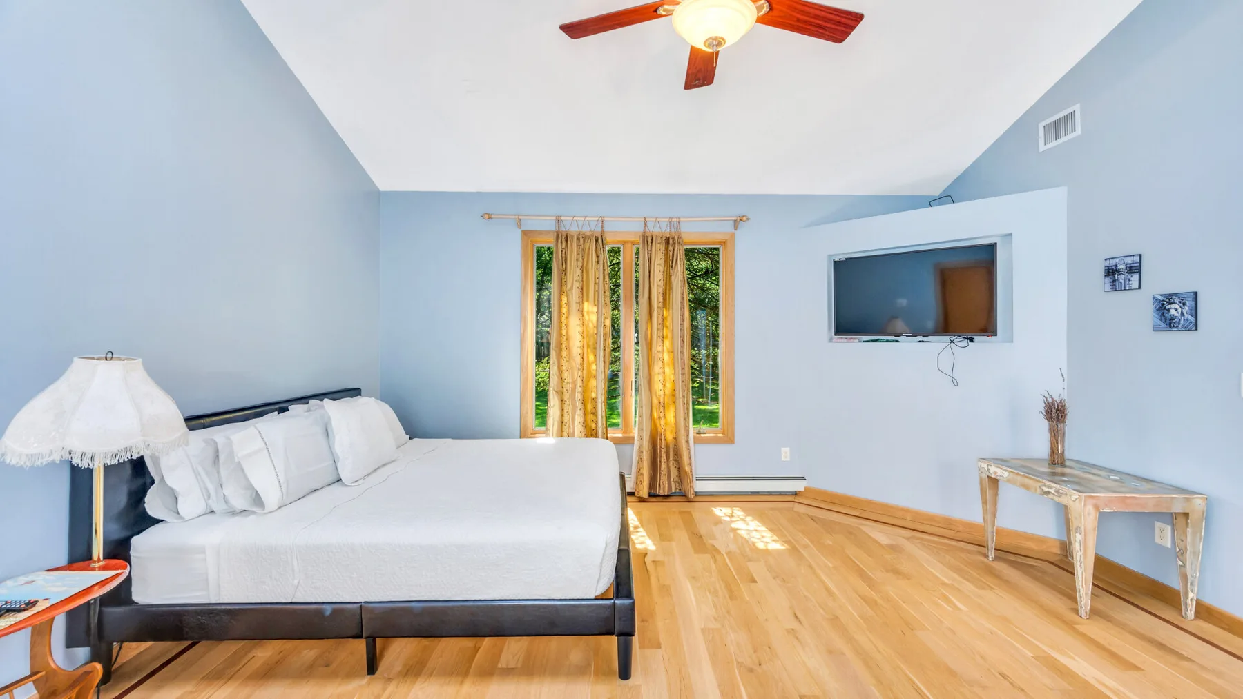 Un dormitorio luminoso con una cama, una ventana con cortinas y un televisor en la pared.