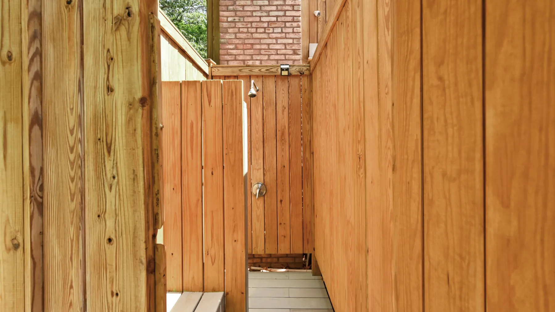 Una zona de ducha exterior estrecha rodeada por una cerca de madera.