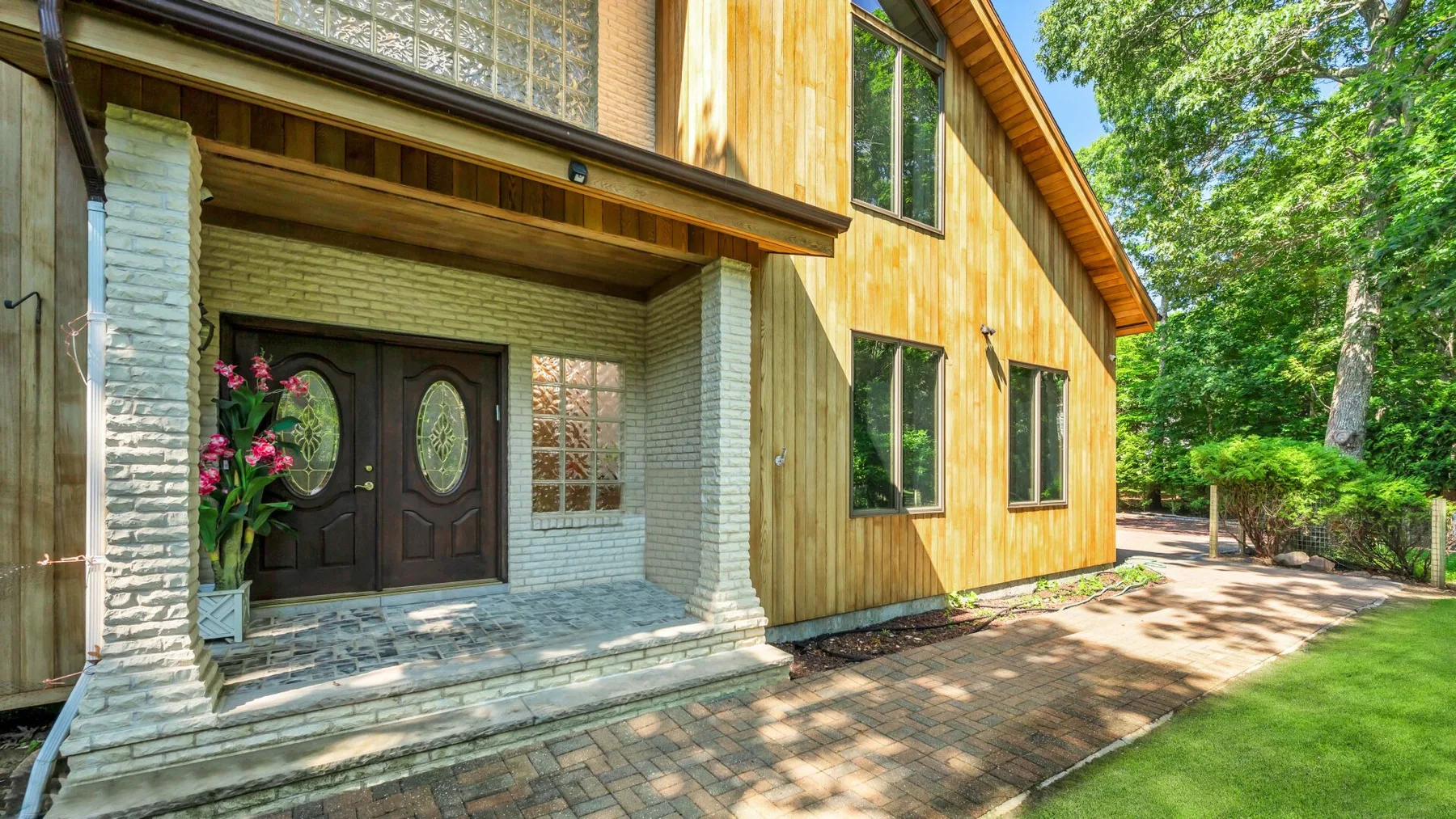 Entrada de una casa revestida de madera, con puertas dobles oscuras y un sendero pavimentado.