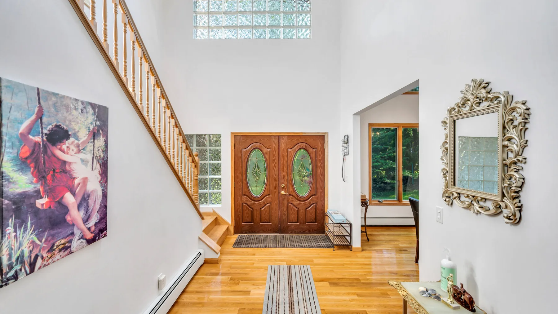 Una entrada luminosa con una escalera de madera, puertas dobles y un tapete en el suelo.