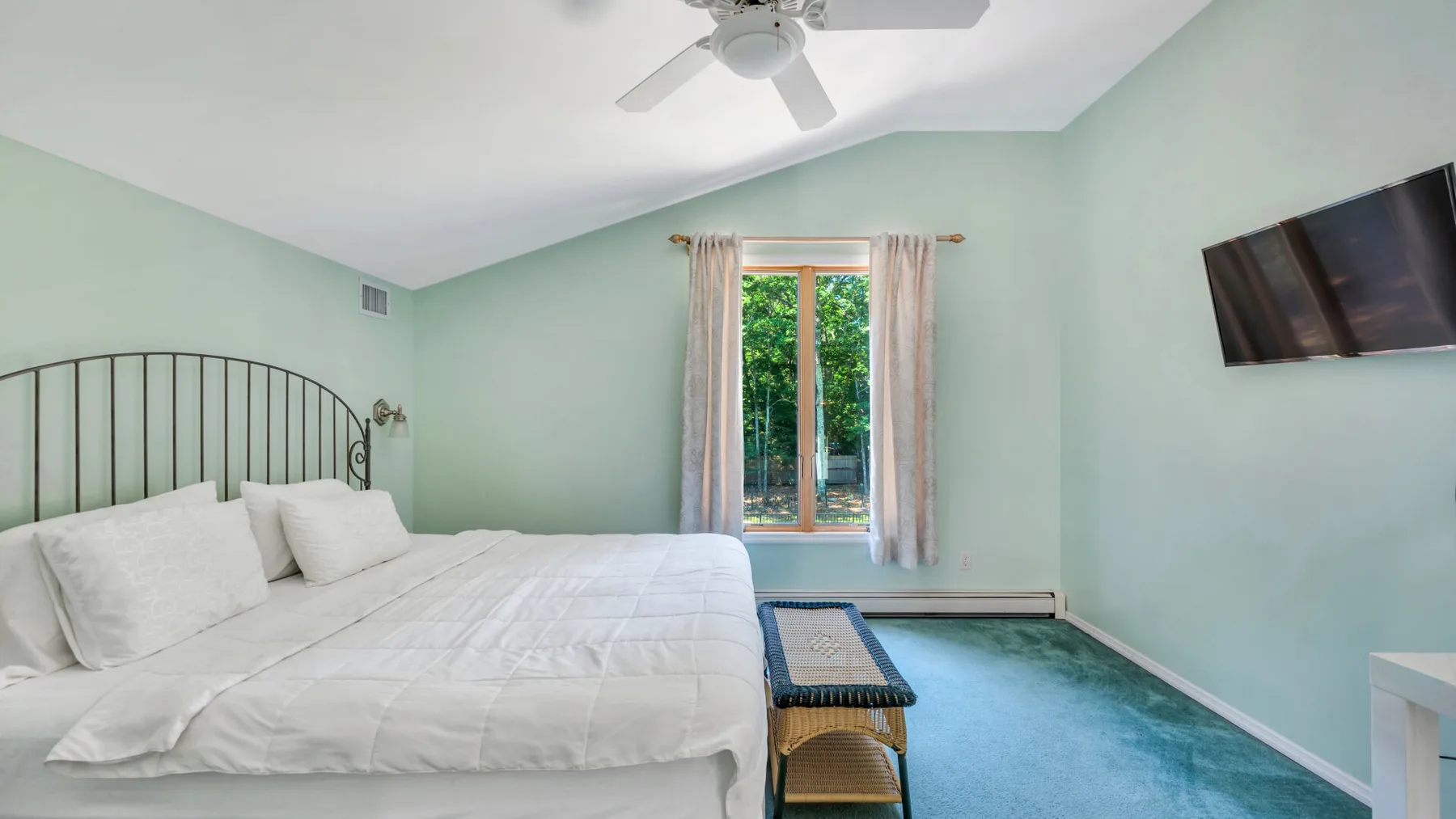 Un dormitorio con una cama grande, alfombra azul y una ventana con vistas a la vegetación.