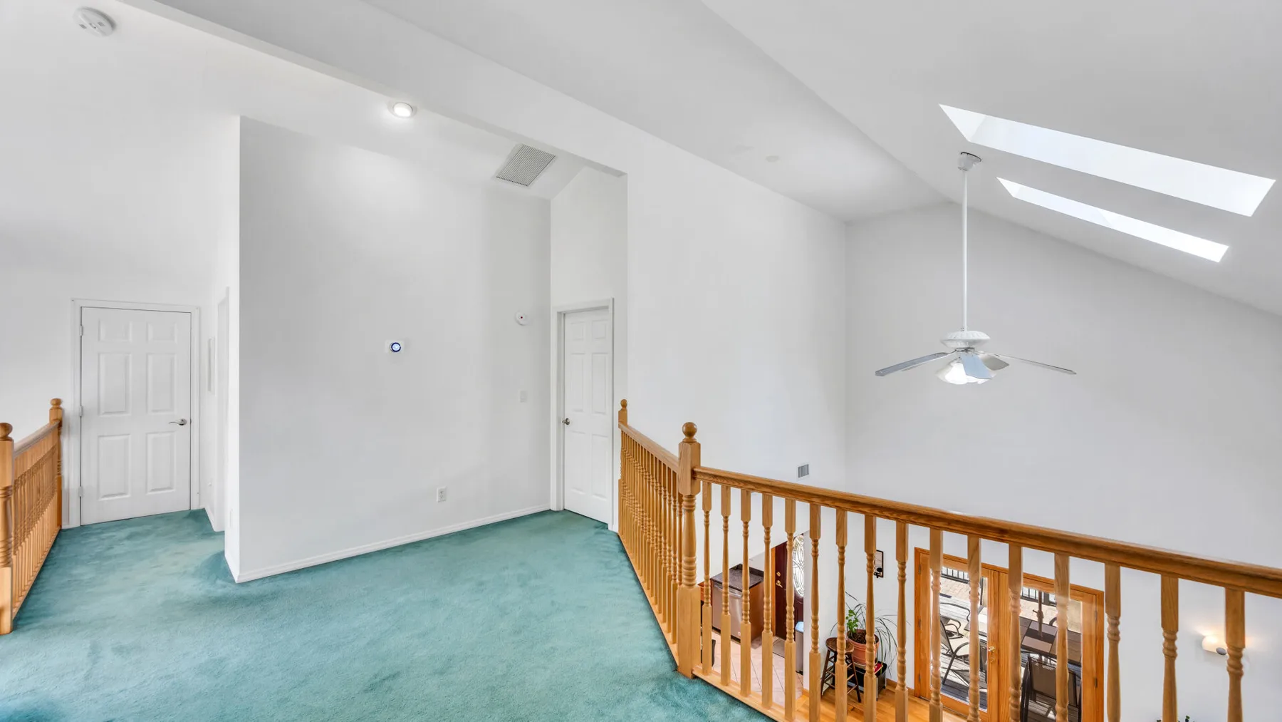 Un rellano luminoso con barandillas de madera y tragaluces inclinados.