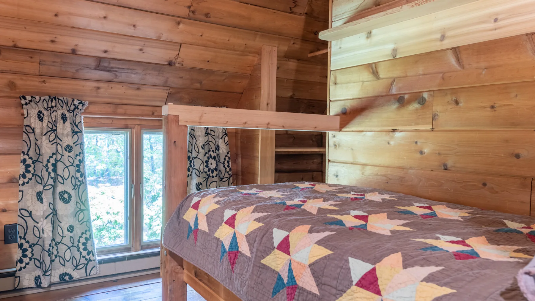 Dormitorio revestido de madera con una cama elevada cubierta por una colcha colorida.