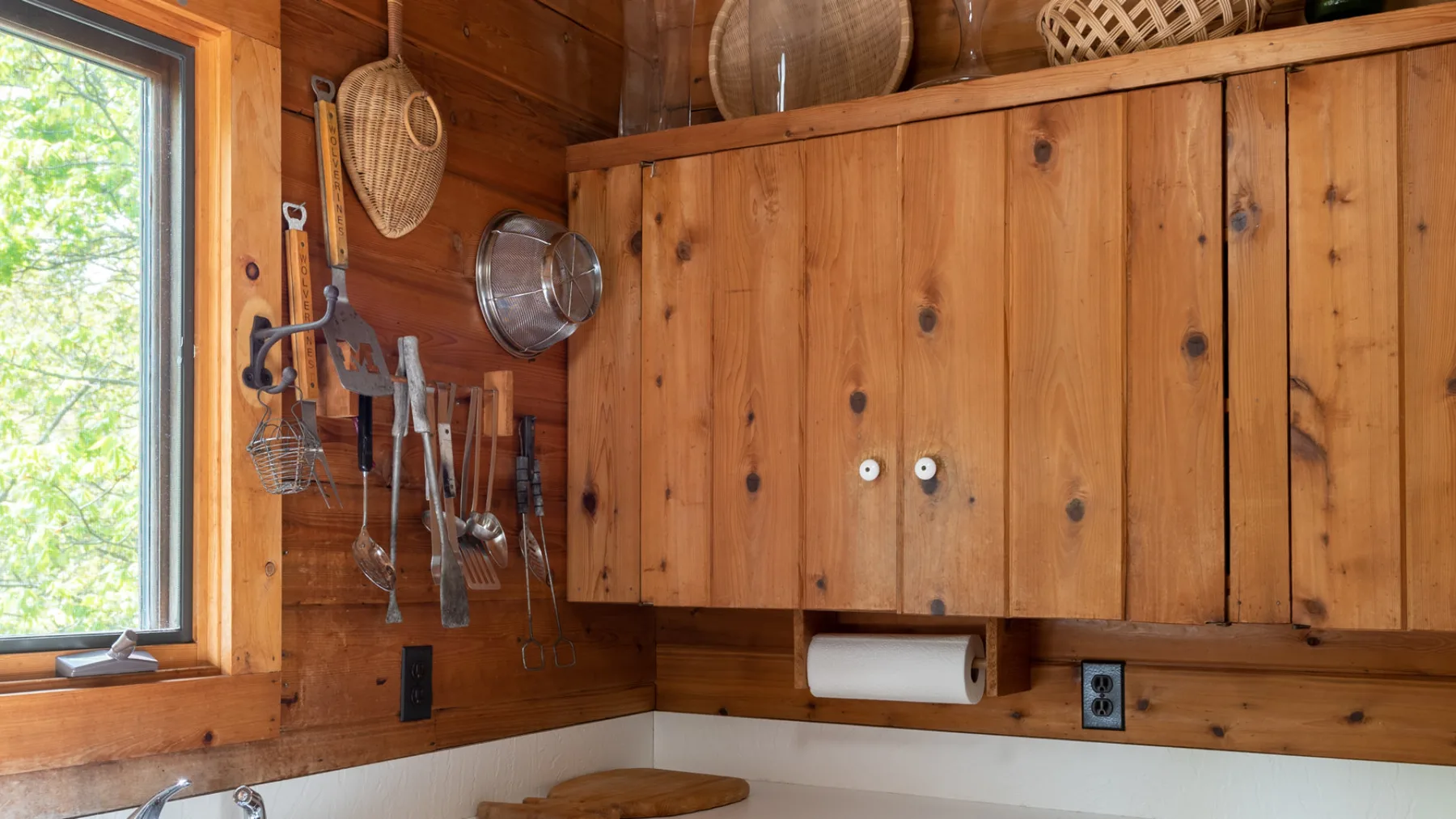 Una pared de cocina revestida de madera, con utensilios colgantes y una ventana.
