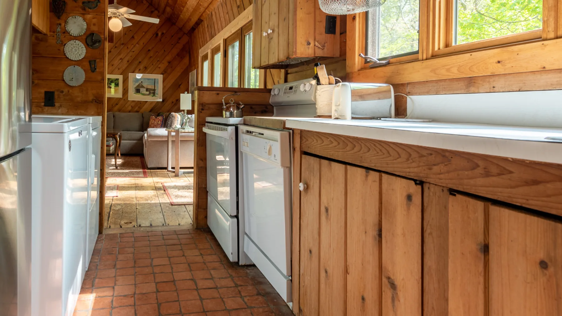 Una cocina revestida de madera, con electrodomésticos y una encimera larga bajo las ventanas.