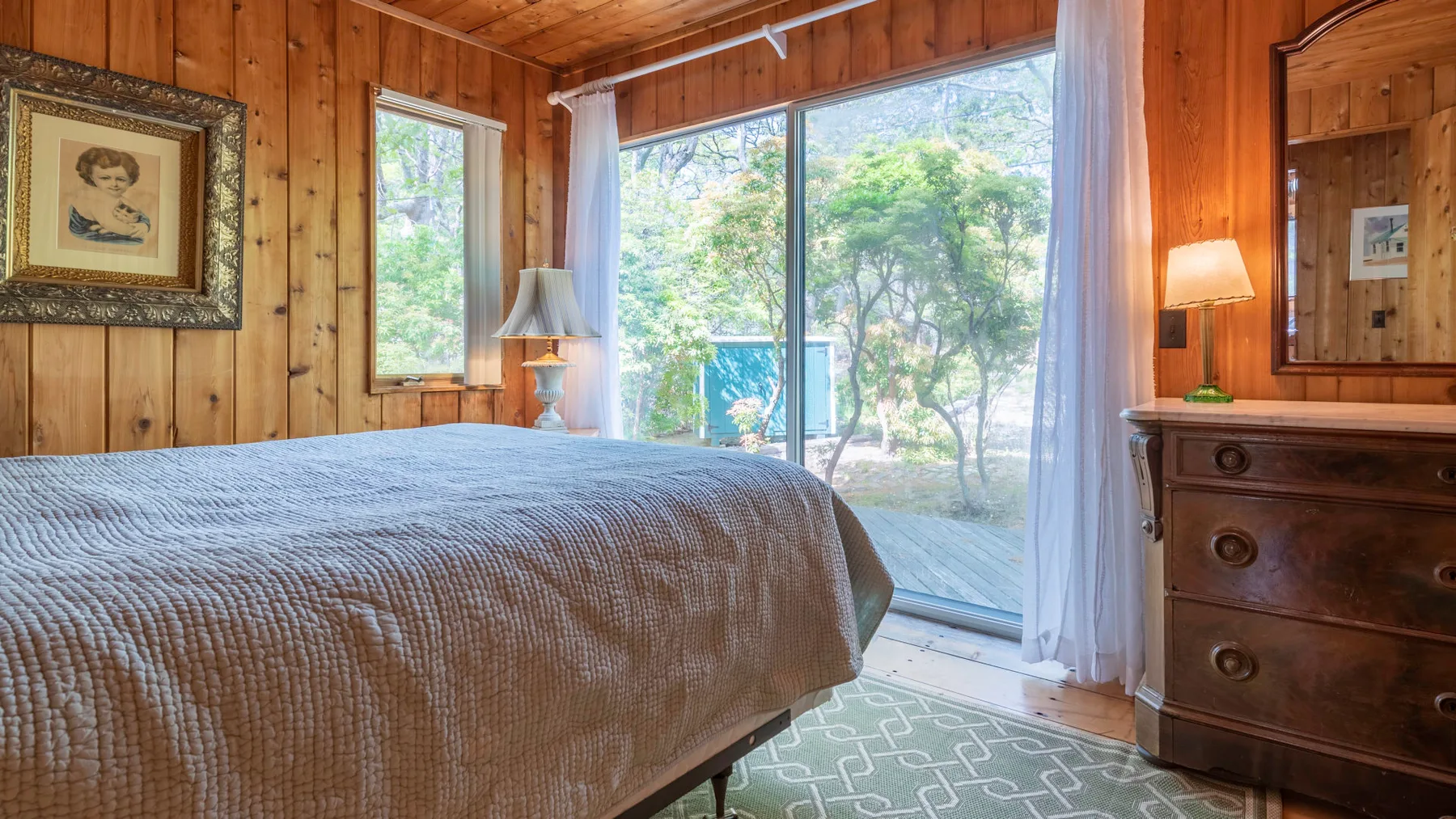 Un dormitorio con una cama junto a grandes ventanas que dan a una frondosa vegetación.