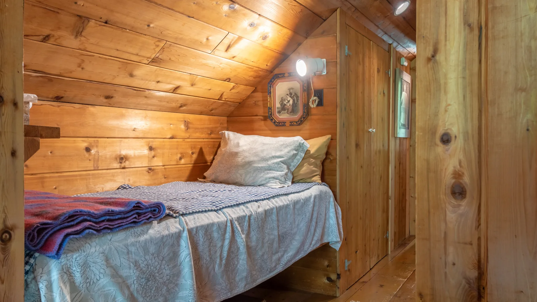 Una cama está bajo un techo inclinado de madera en una habitación revestida de madera.