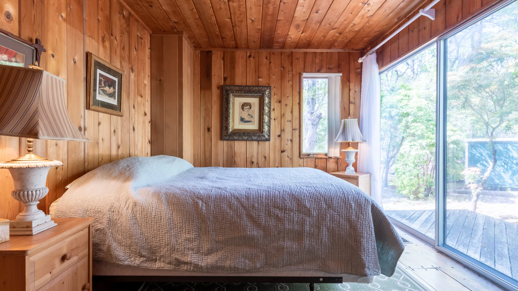 Un dormitorio con una cama junto a grandes ventanas con vista a los árboles.