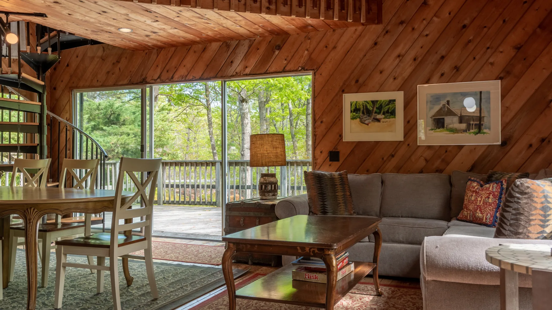 Una sala-comedor revestida de madera tiene un sofá, una mesa de comedor y ventanas con vista a los árboles.