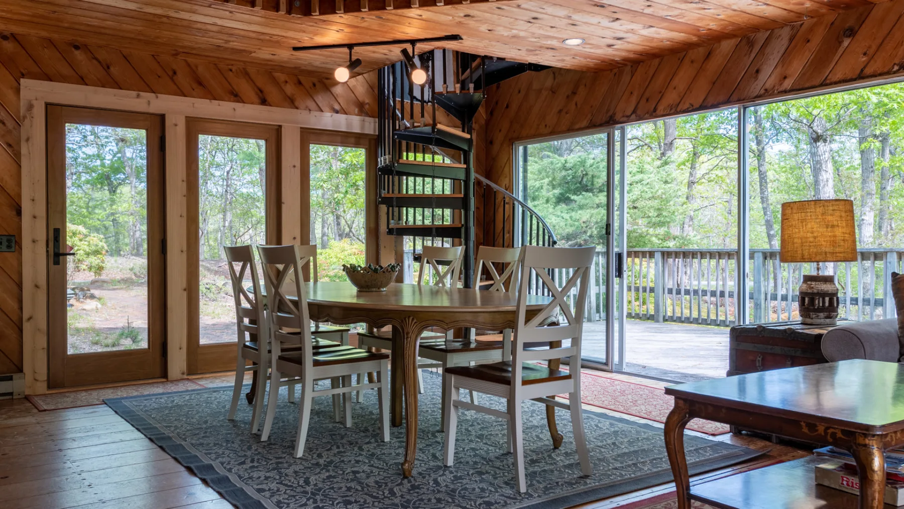 Un comedor con una mesa de madera y sillas junto a grandes ventanales.