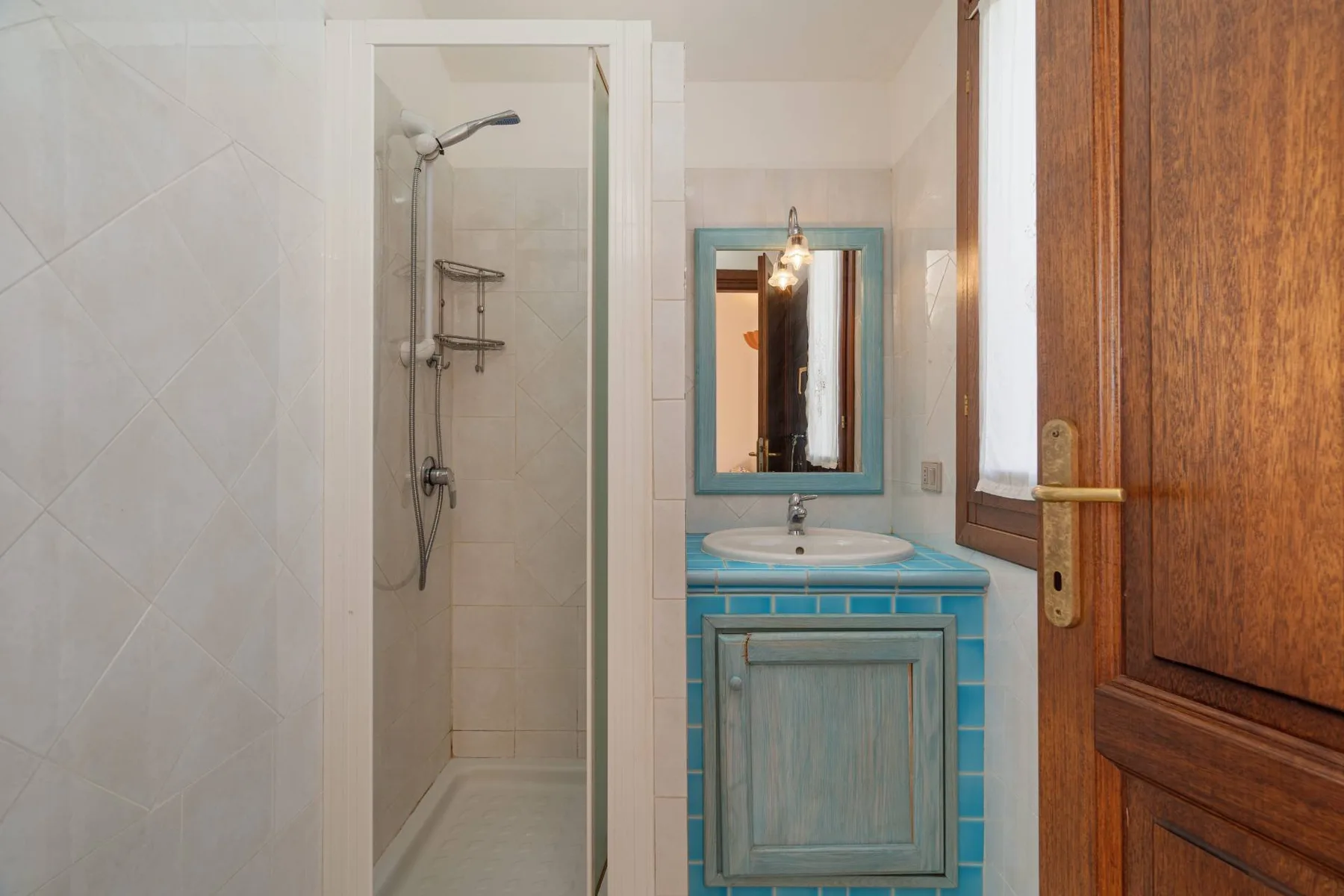 Un baño con ducha de cristal, lavabo azul y espejo de pared.