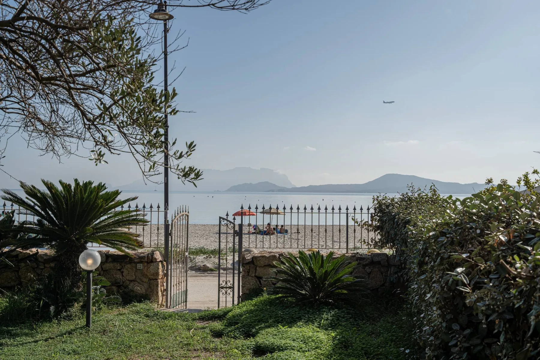 Una puerta del jardín da a una playa de arena y aguas tranquilas.