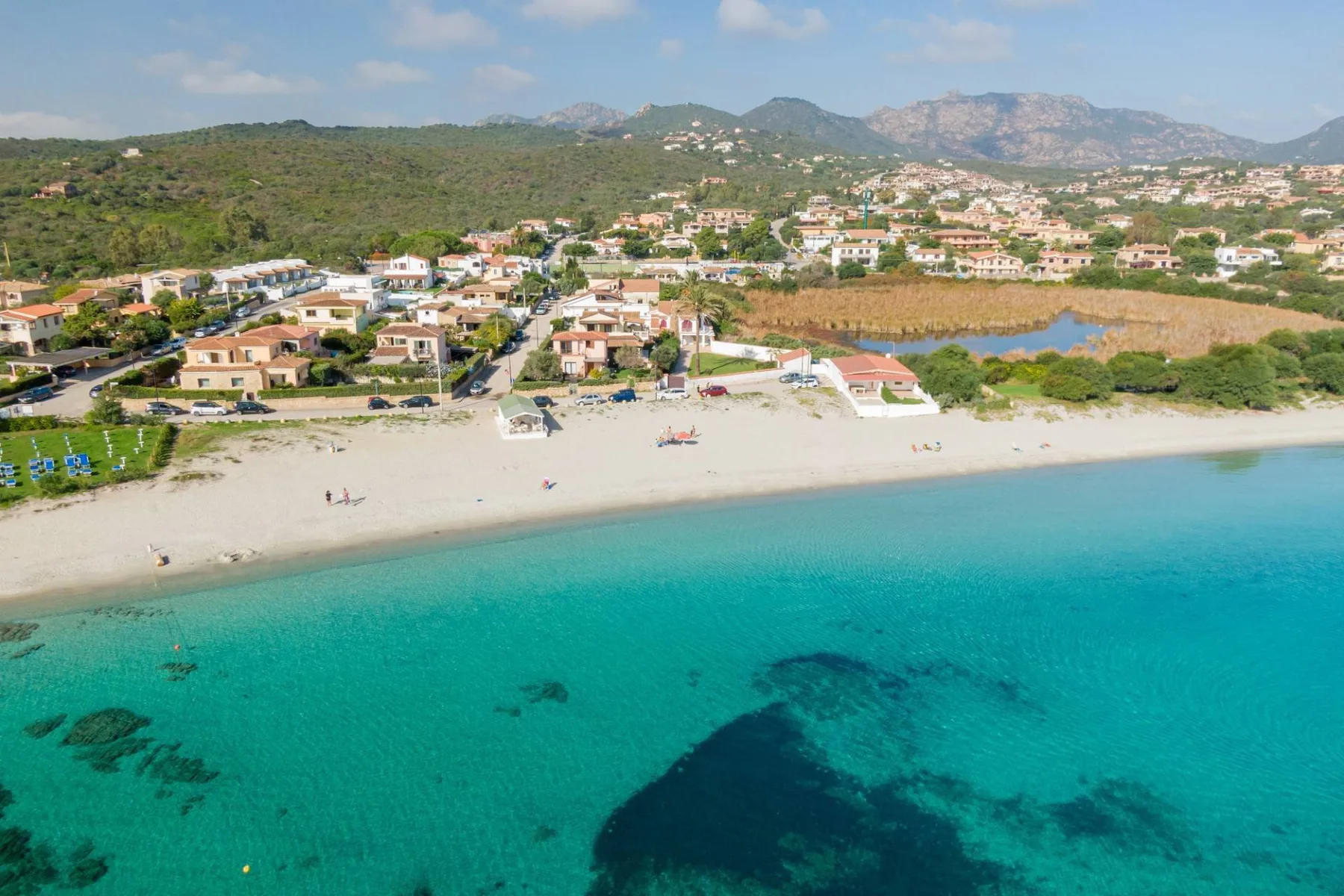 Vista aérea de una playa de arena con aguas turquesas y un pueblo costero.