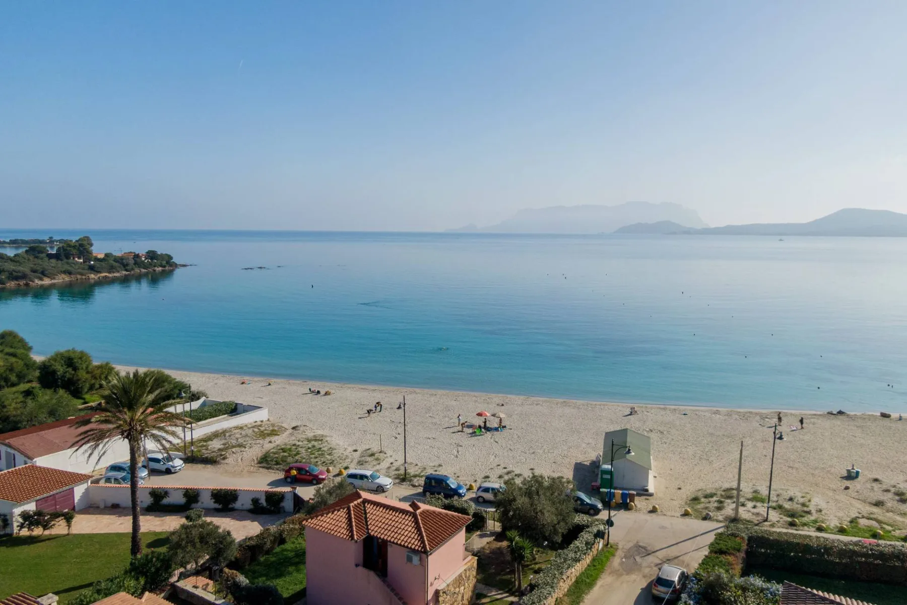 Una playa junto al mar y aguas azules tranquilas se extienden hacia montañas lejanas.