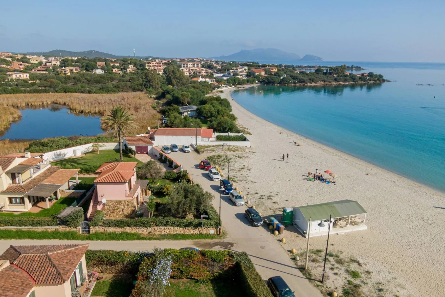 Vista aérea de una playa curva junto a casas costeras y aguas tranquilas.