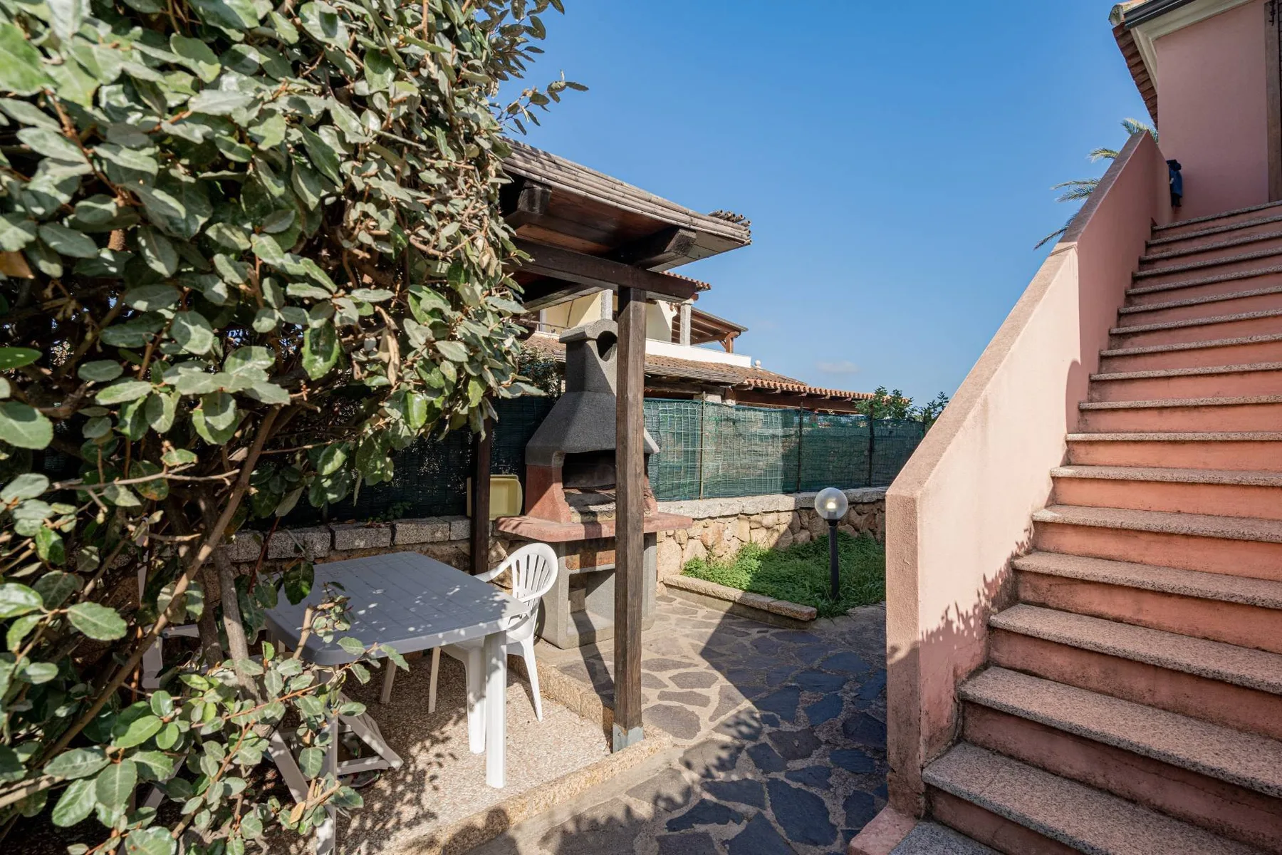 Un patio pavimentado tiene una mesa y asientos junto a una zona cubierta con parrilla.