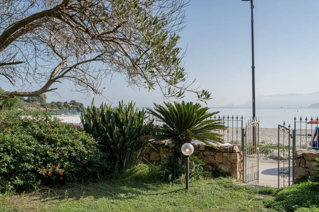 Un jardín junto al mar con plantas frondosas, un muro de piedra y vistas al agua.