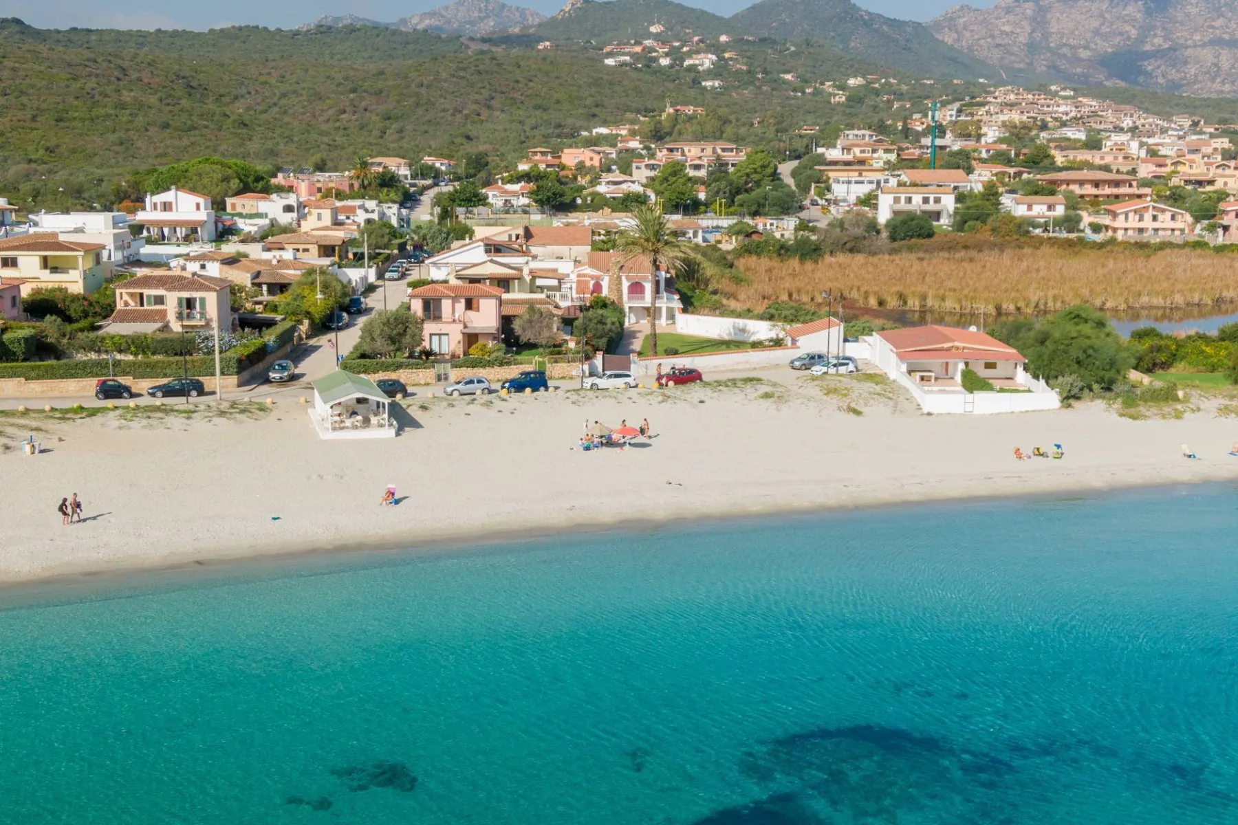Vista aérea de una playa de arena y aguas turquesas junto a un pueblo costero.