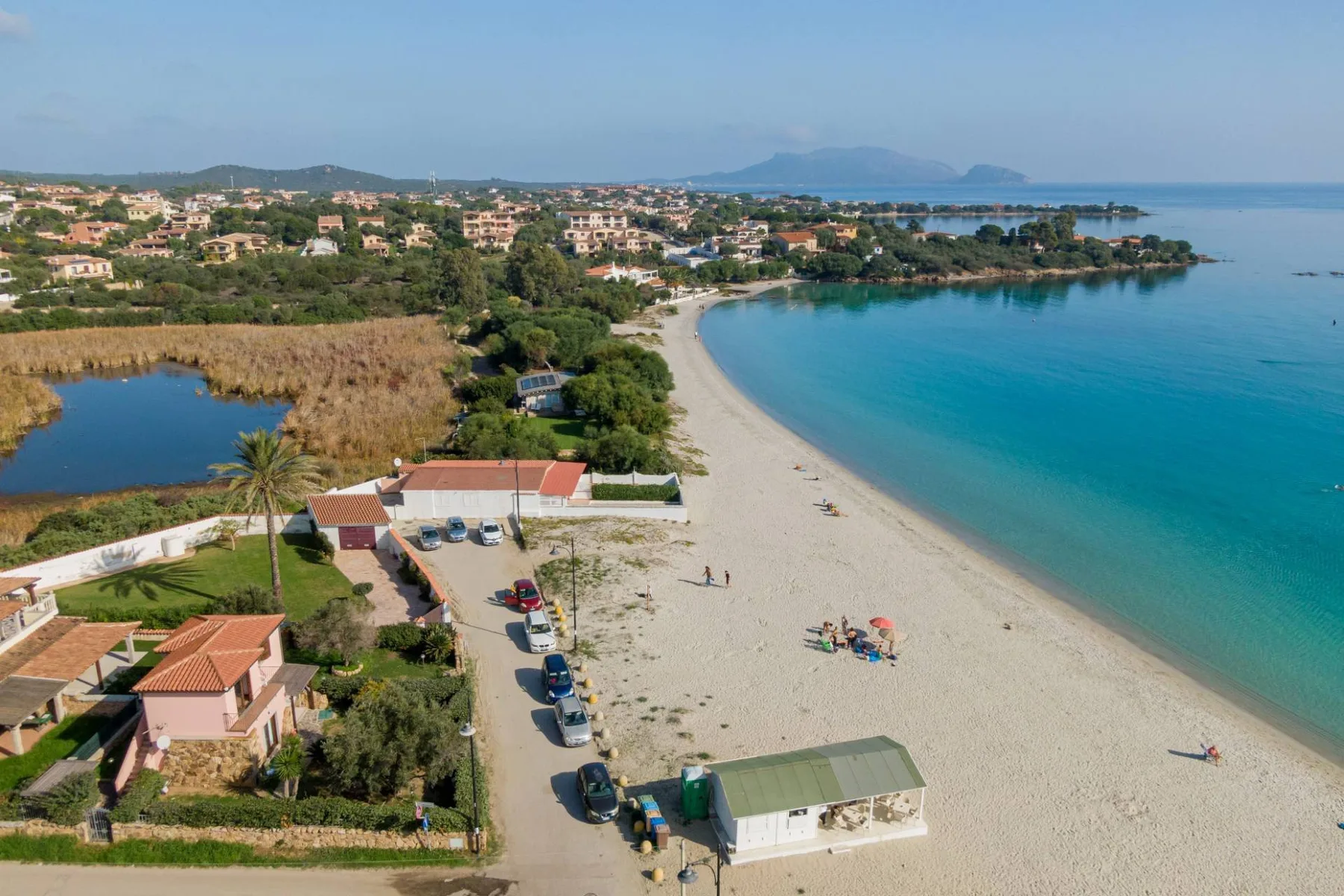 Vista aérea de una playa de arena curva junto a aguas turquesas y casas costeras.