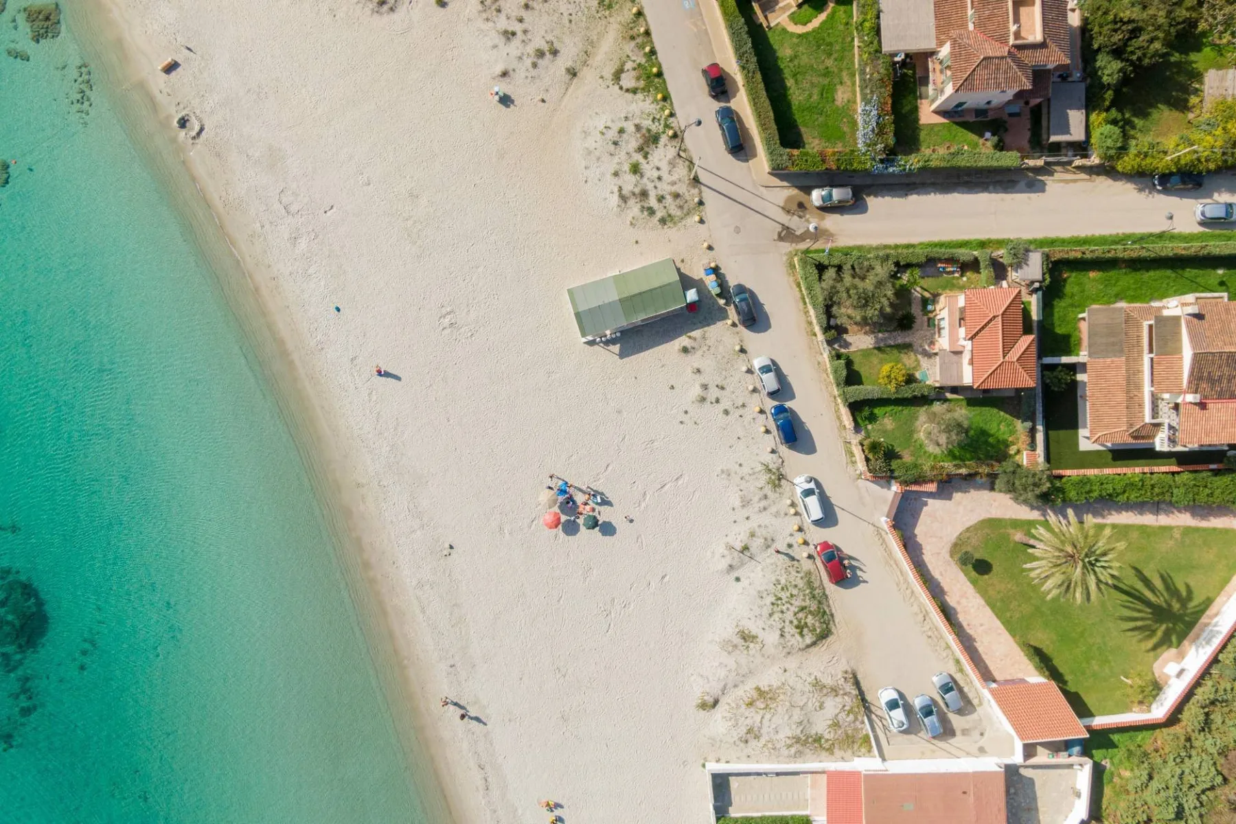 Vista aérea de una playa de arena junto a aguas turquesas y casas cercanas.