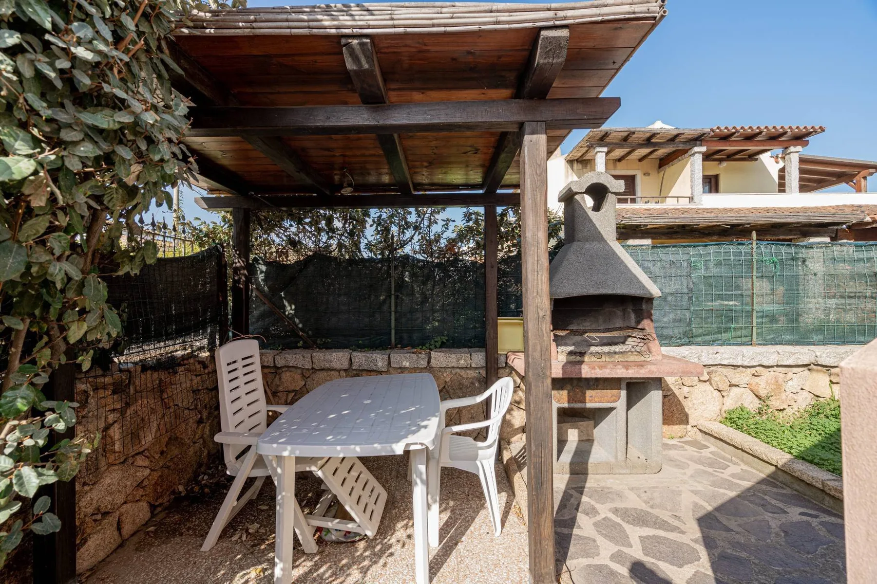Un patio exterior cubierto con una mesa, sillas y una parrilla de obra.