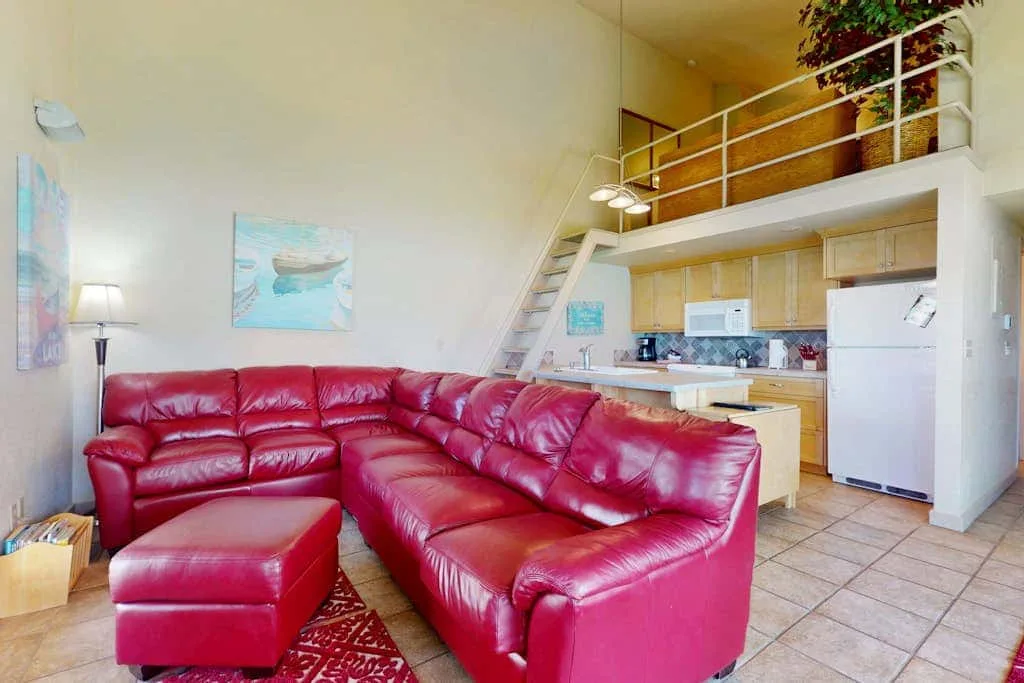Una sala de estar con asientos rojos y una cocina compacta bajo un altillo.
