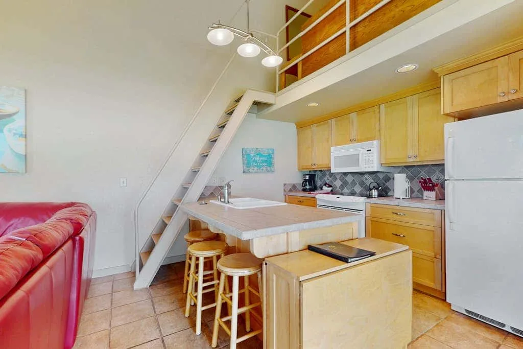 Una cocina y zona de comedor compactas con barra, taburetes y escaleras a un altillo.