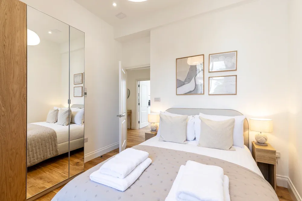 A bright bedroom with a neatly made bed and mirrored wardrobe doors.
