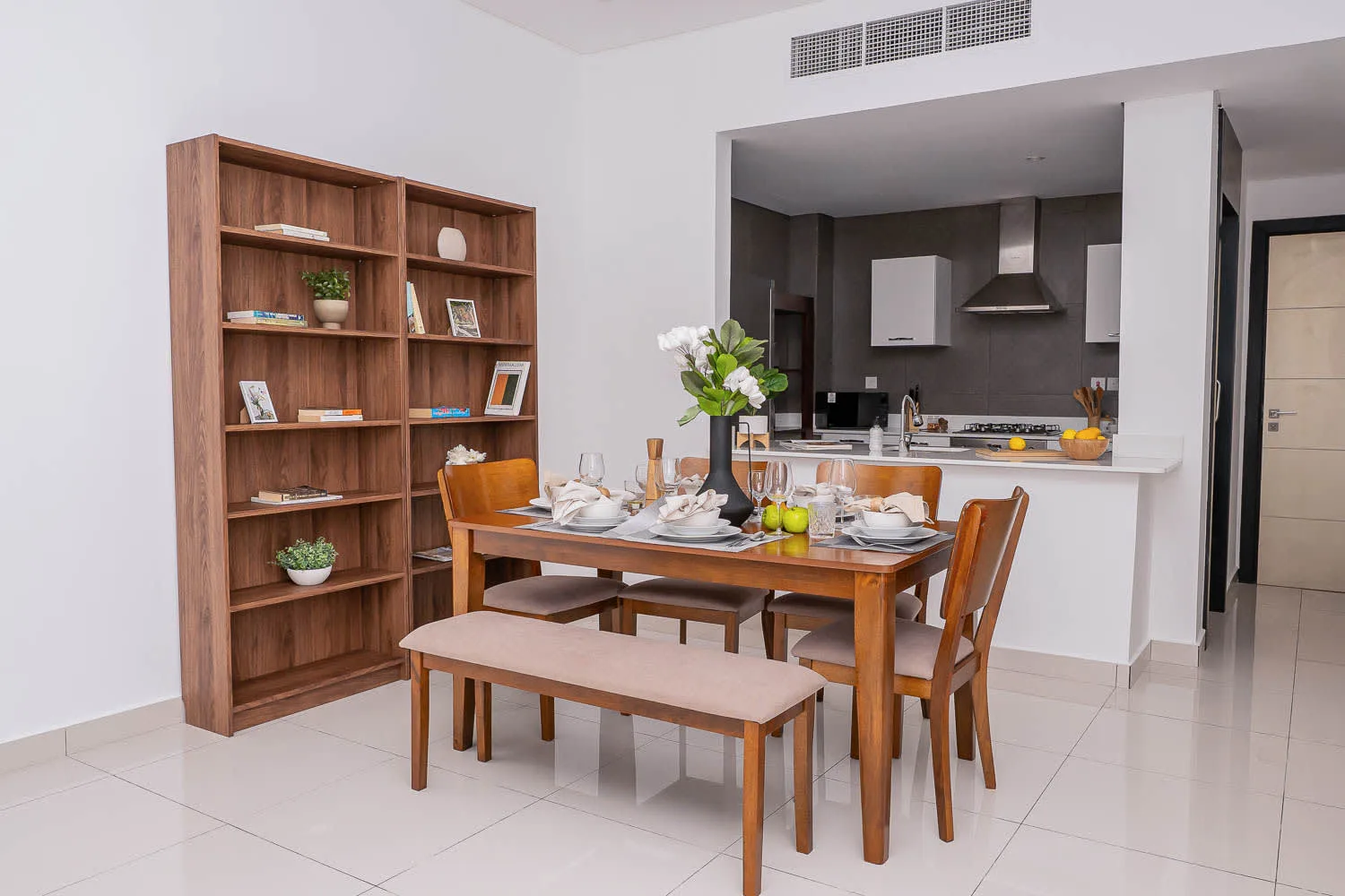 A dining area with a wooden table and bench beside an open kitchen.