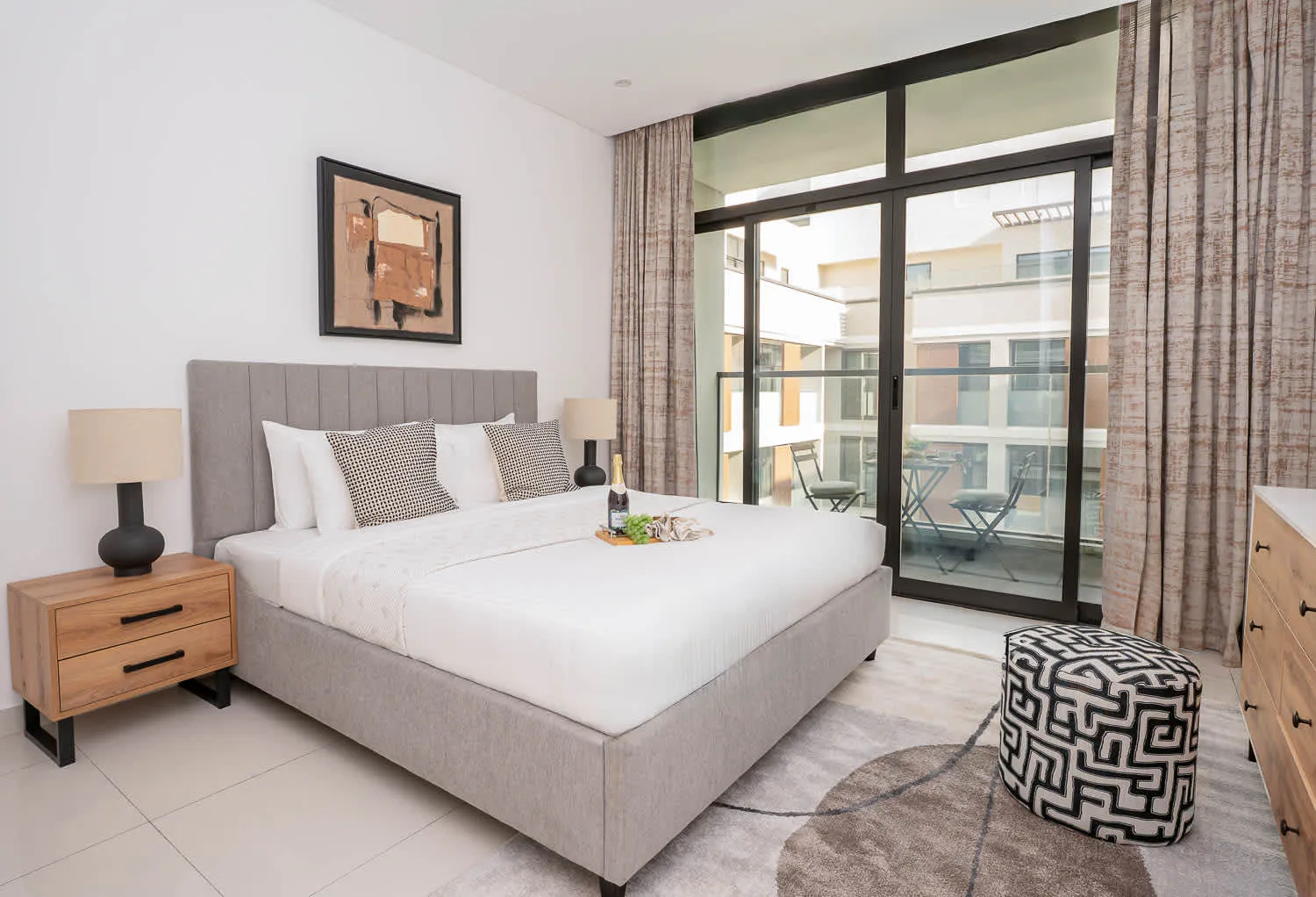 A bedroom with a large bed beside floor-to-ceiling windows overlooking a balcony.