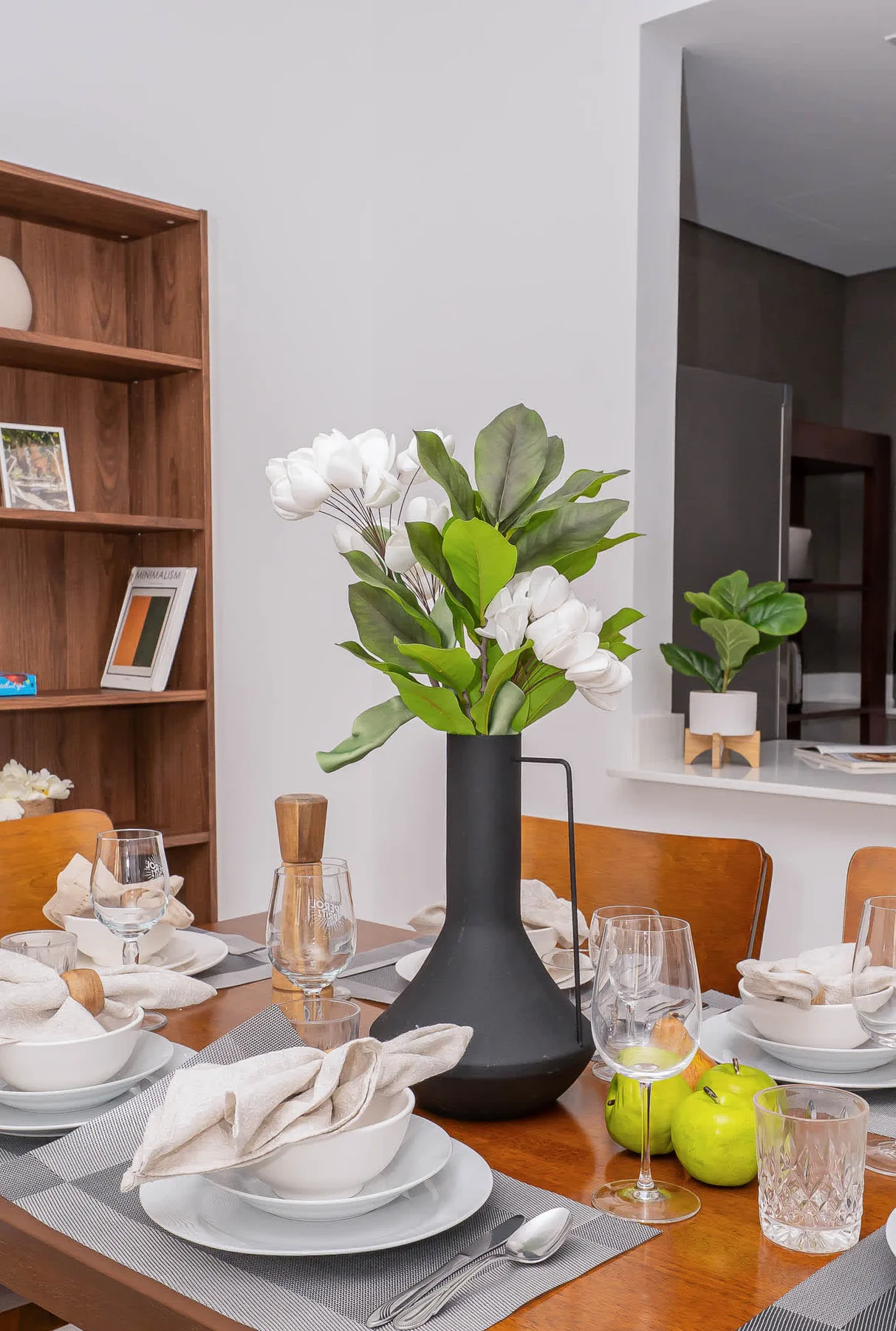 A dining table is set with dishes, glassware, and a vase of flowers.