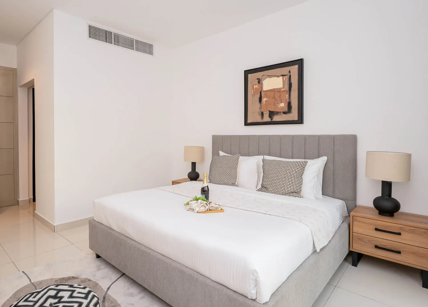 A neatly made bedroom features a large bed with a gray upholstered headboard.