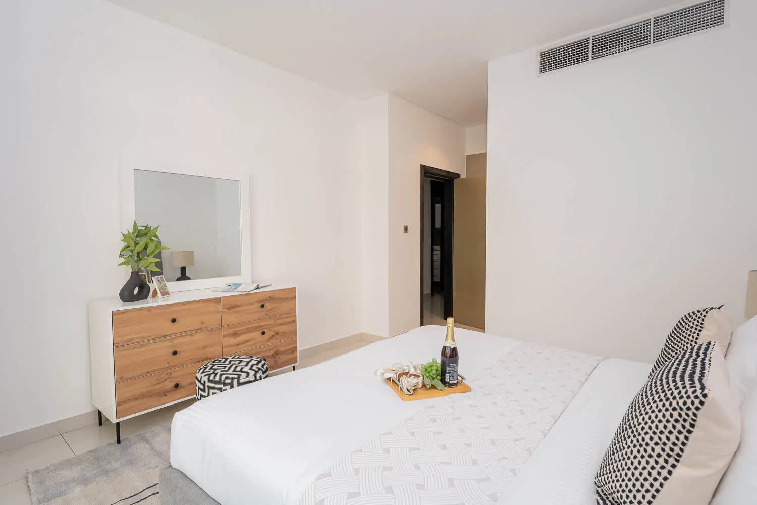 A bright bedroom with a bed and a wooden dresser beneath a mirror.