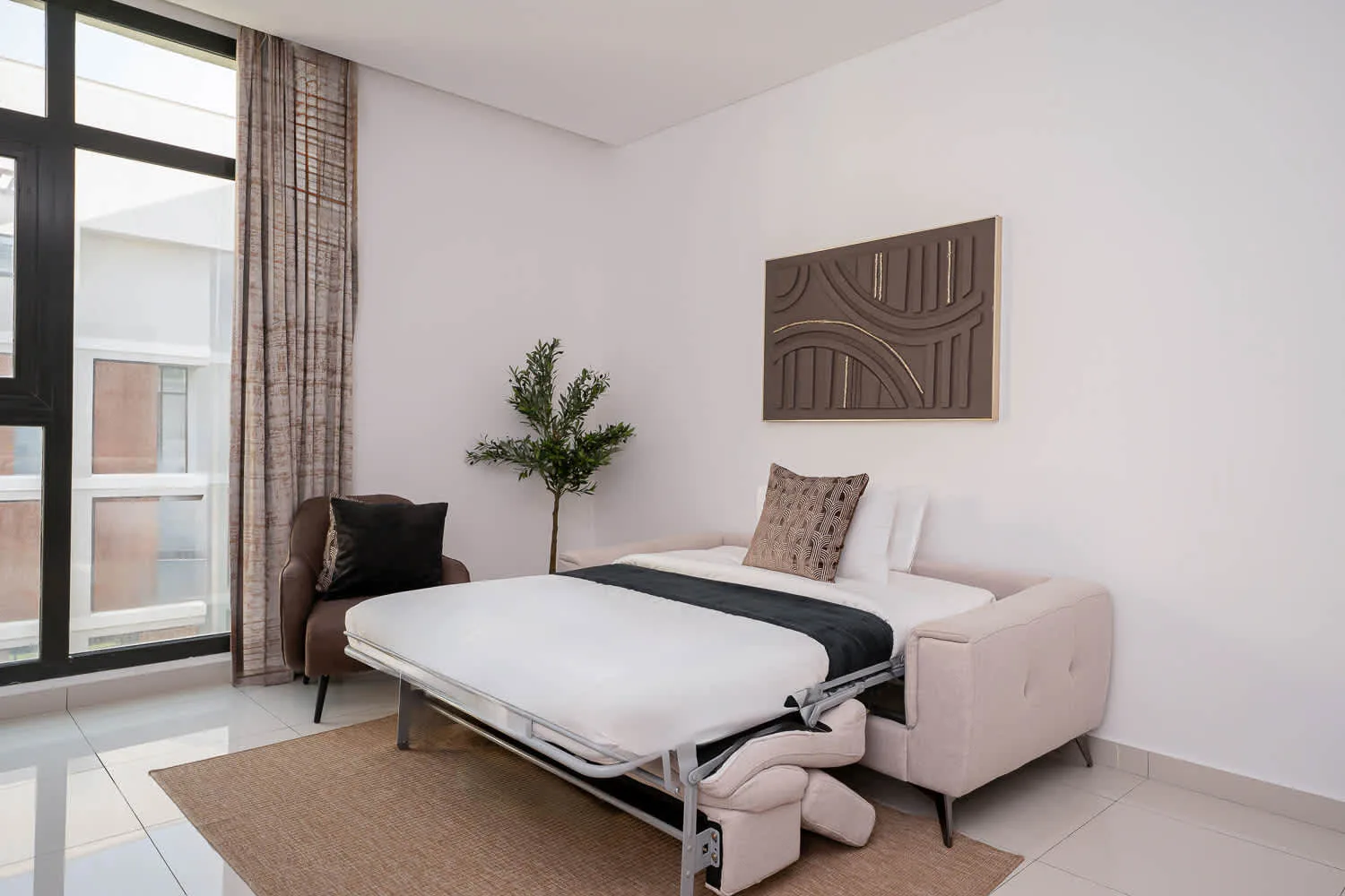 A bright bedroom with a bed, a small tree, and large windows.