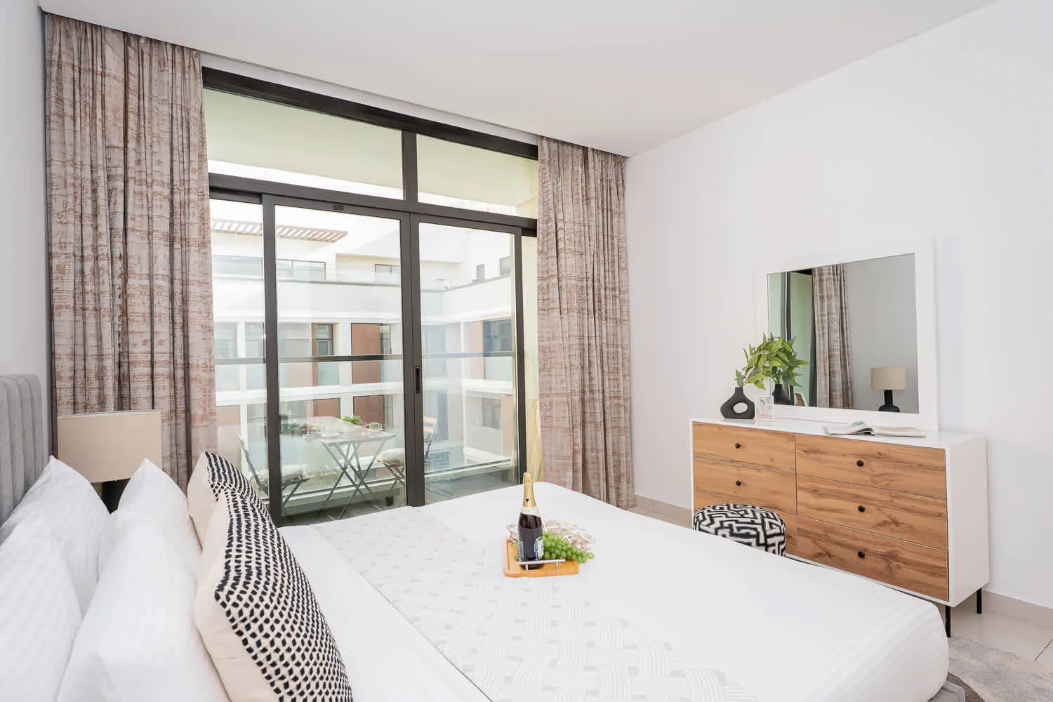 A bright bedroom with a large bed, bedside lamp, and glass doors opening to a balcony.