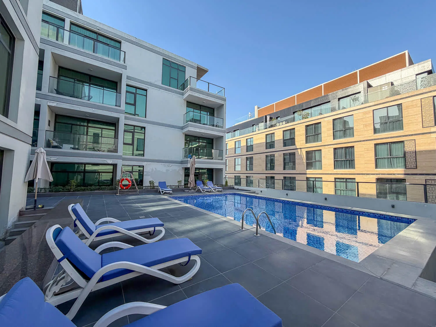 An outdoor swimming pool sits beside modern multi-story buildings.