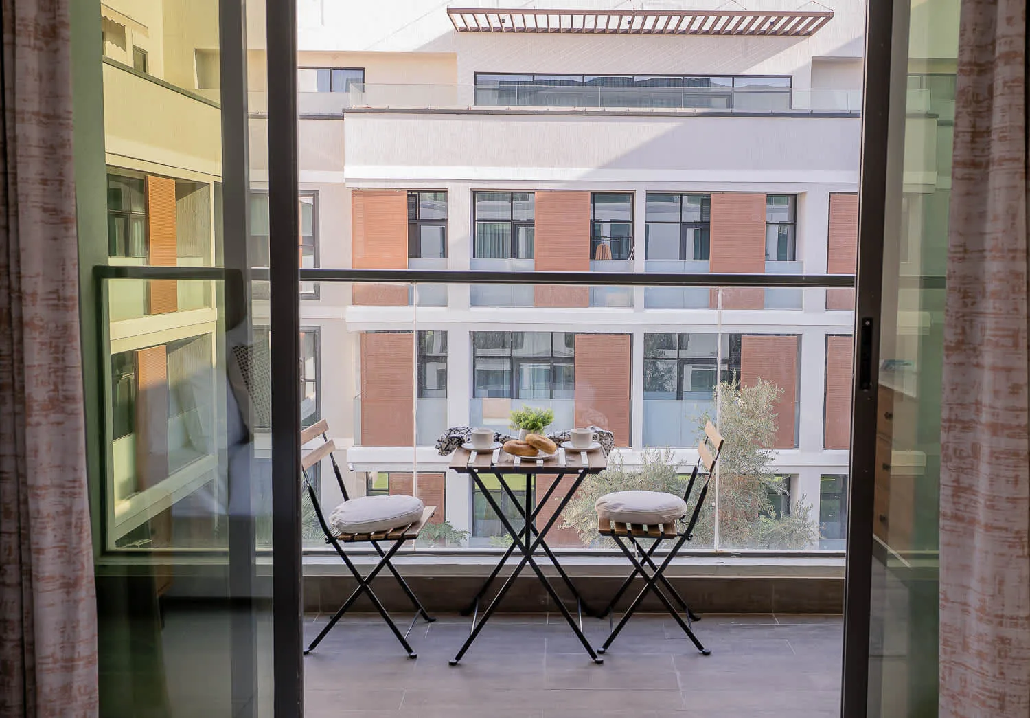 A small balcony has a table and seating overlooking a neighboring building.