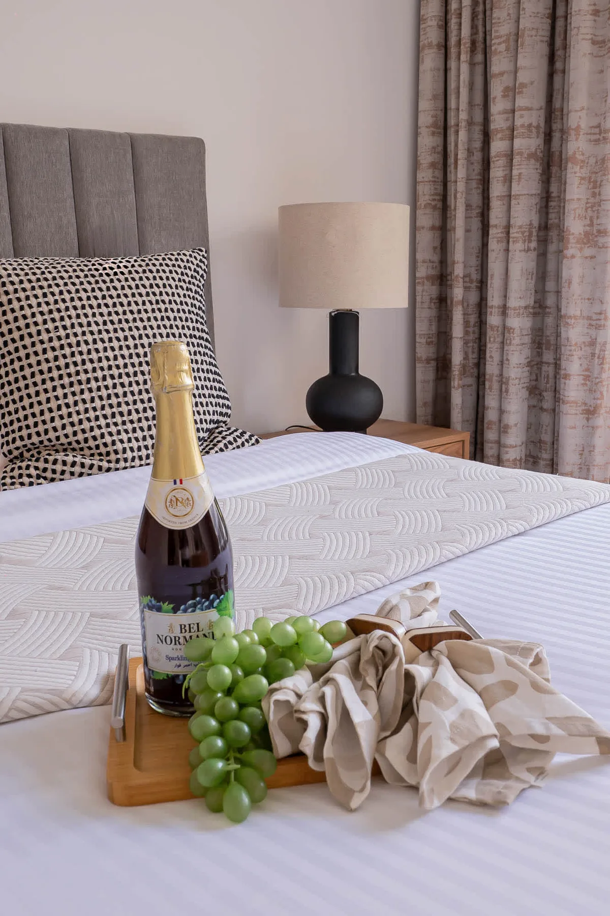 A bedroom with a neatly made bed, bedside lamp, and grapes on a tray.