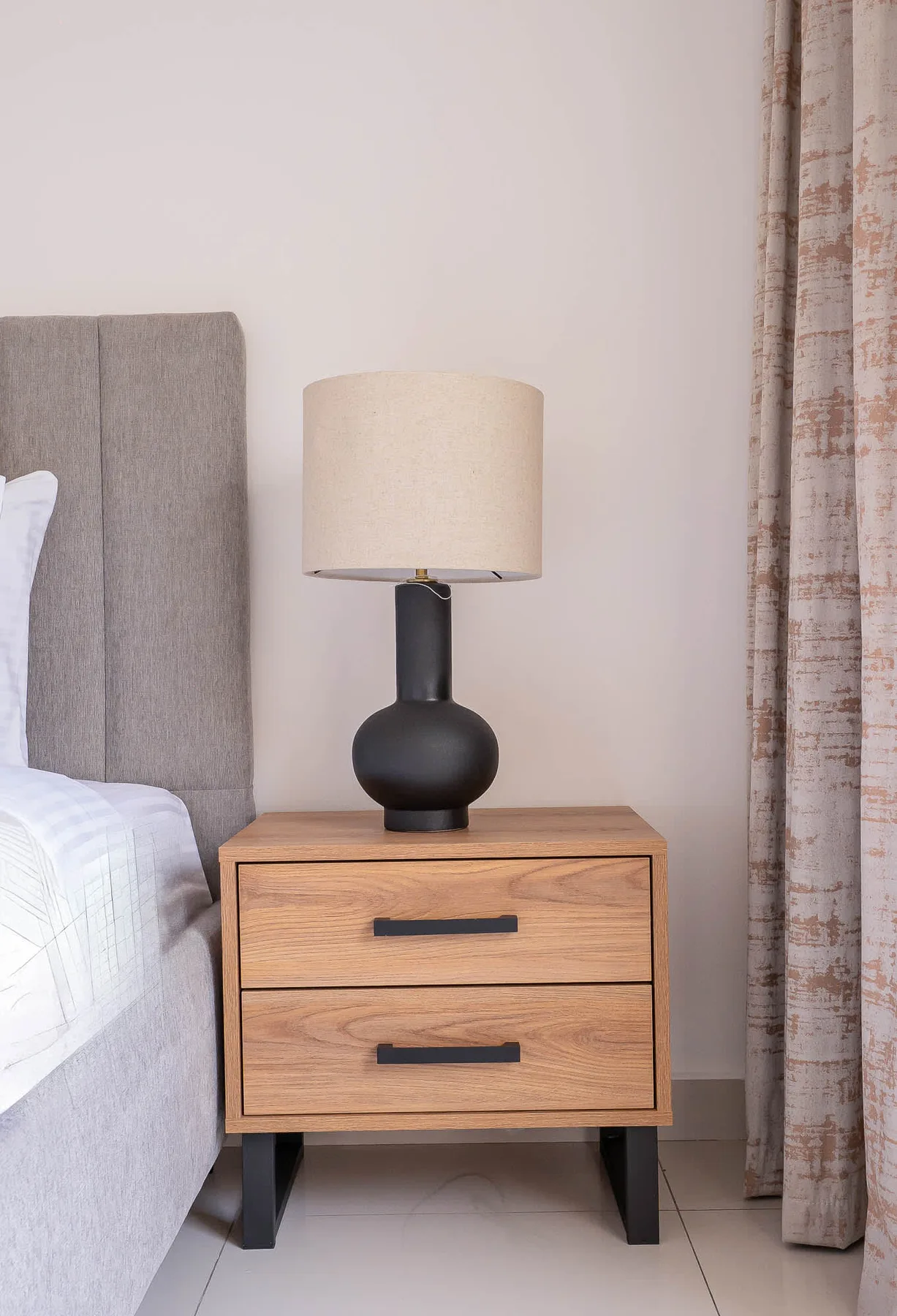 A bedside table with a lamp stands beside a bed.