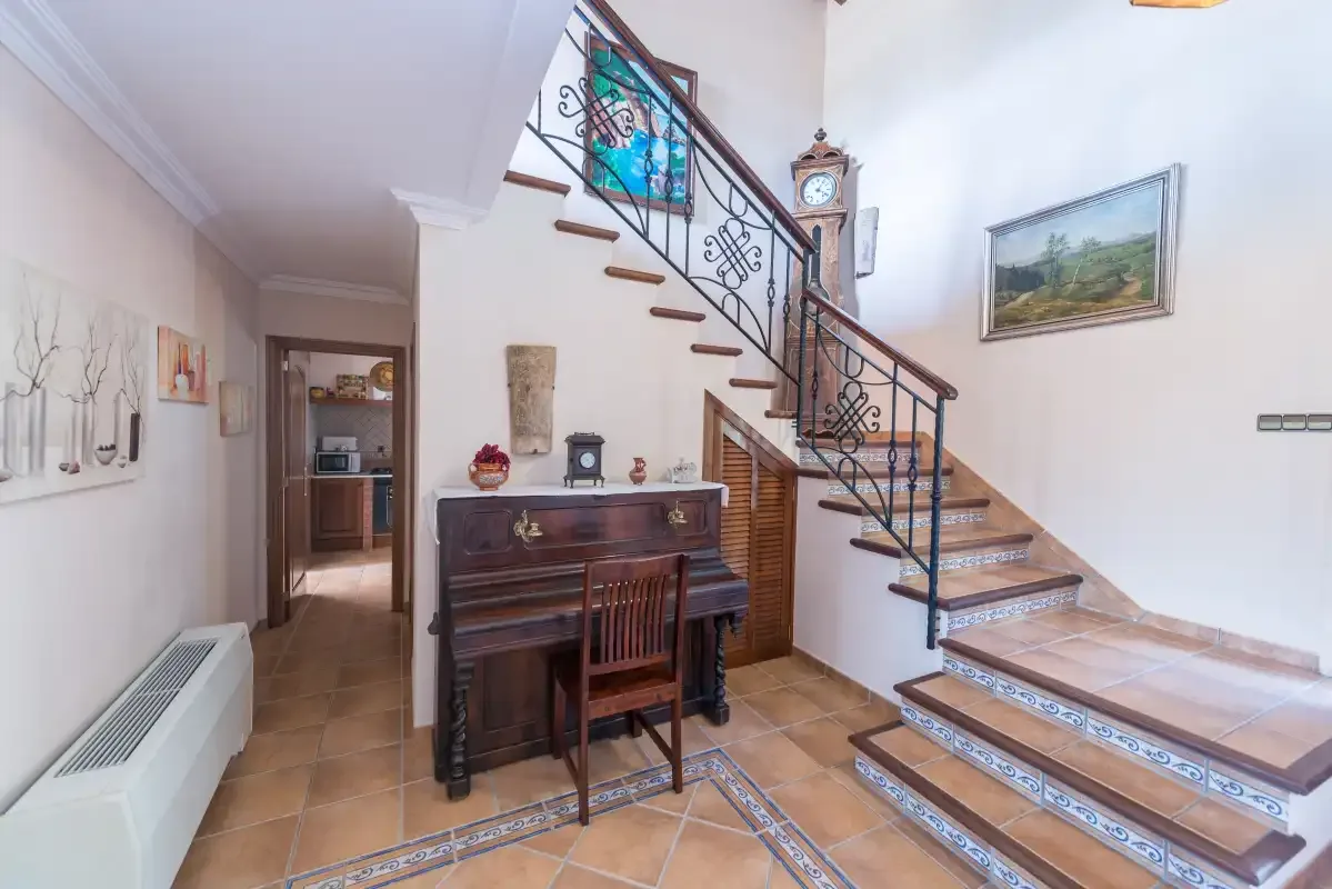 An interior hallway features a staircase beside a wooden upright piano.