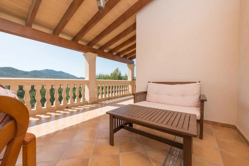 A covered terrace with a cushioned seating area and views of hills beyond the railing.