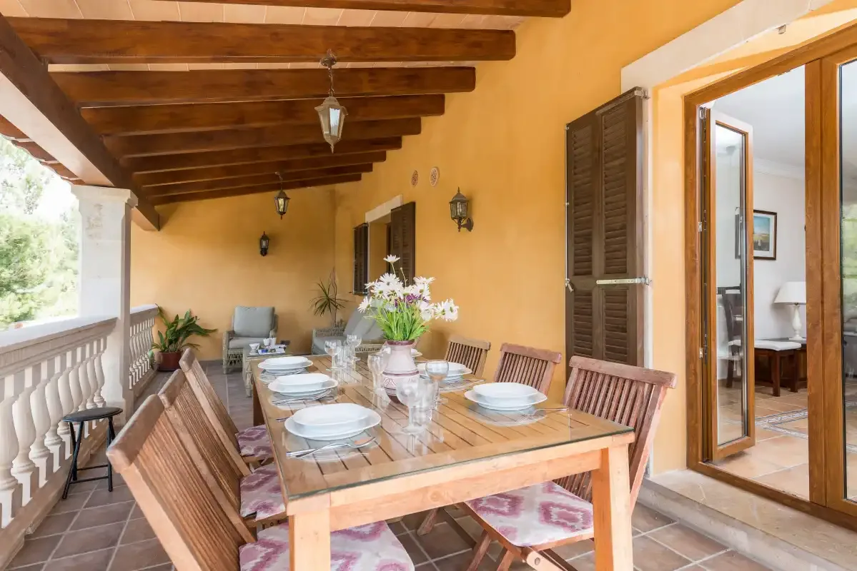 A covered terrace dining area with a long table and wooden seating.